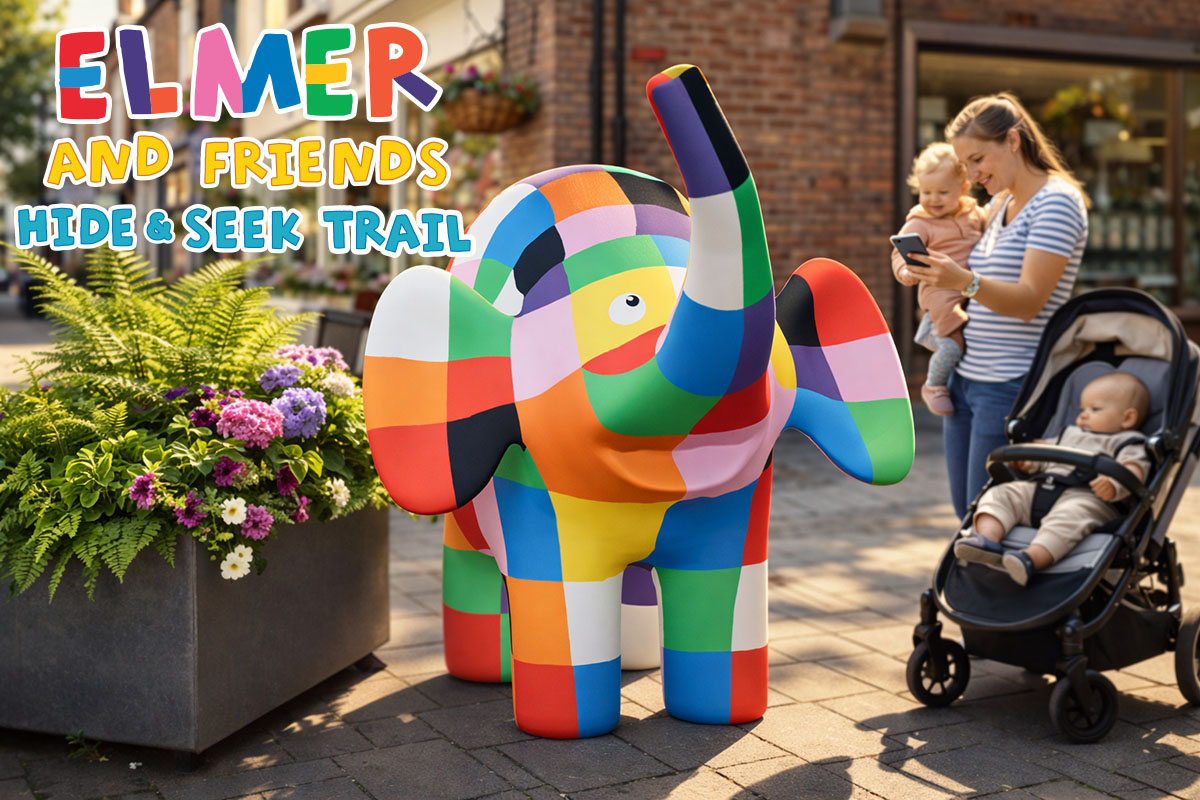 A mother carrying a baby looks at her phone next to a large colourful Elmer the elephant in an outdoor shopping area