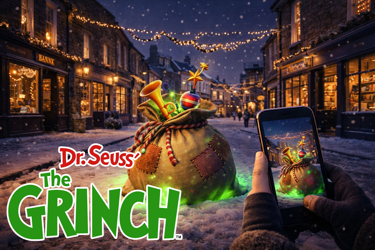 A hand holds a phone scanning a Grinch trail marker on a snowy Christmas high street at night